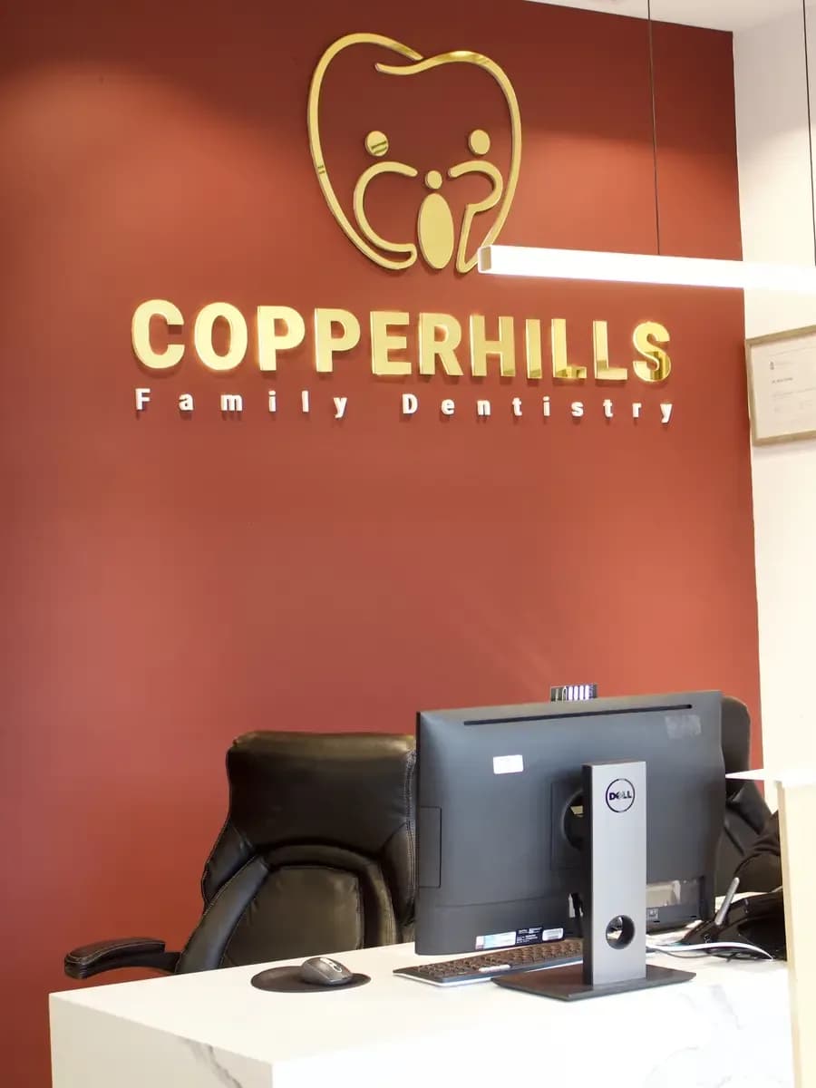 The Copperhills Family Dentistry reception desk beneath the gold logo wall
